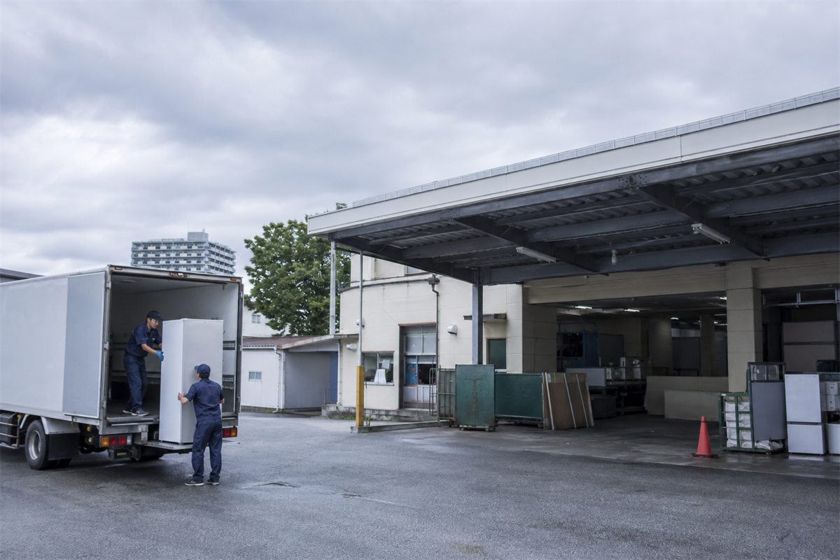 指定引取場所で車両から冷蔵庫を降ろす準備をする場面